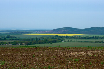 The top view on a valley among the Balkan mountains in spring, the beautiful view of plowed field on the background of village, yellow rapeseed fields and mountains.