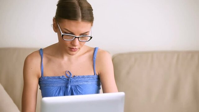 Pretty young casual woman using laptop at home, looking at camera smiling, self-employed freelancer distant worker, cheerful beautiful teenage blogger wearing glasses studying e-learning online course