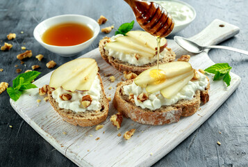 Appetizer bruschetta with pear, honey, walnut and cottage cheese on white board.