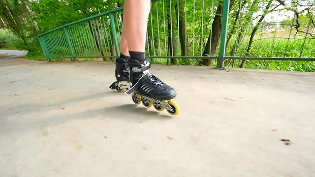 Front close view to inline skates riding on the bridge . Outdoor inline skating on smooth concrete ground on lake bridge. Light skin man in four wheel boots