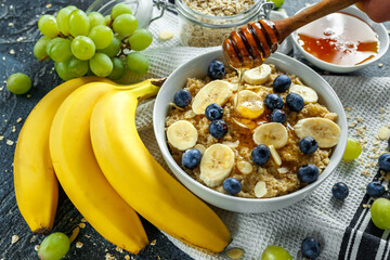Bowl of Healthy Breakfast oatmeal with ripe blueberries, banana, honey, almonds and green grape. Top view