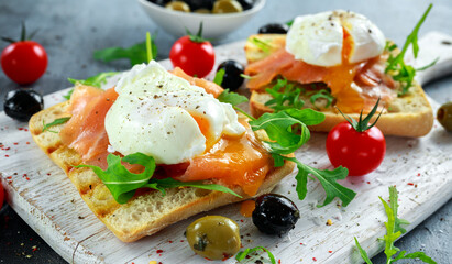 Fototapeta na wymiar Poached egg on grilled toast with smoked salmon, rucola, olives and vegetables on white board. healthy breakfast