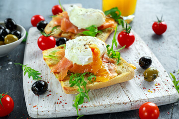 Poached egg on grilled toast with smoked salmon, rucola, olives, vegetables and orange juice. on white board. healthy breakfast