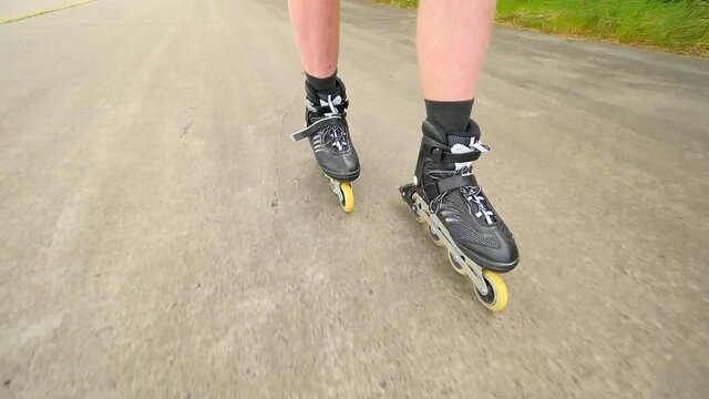 Shuffle inline skating on way in pine forest. Mans legs roller skating on the asphalt in hot summer day. Close up view to quick shuffle movement of four wheels inline boots.
