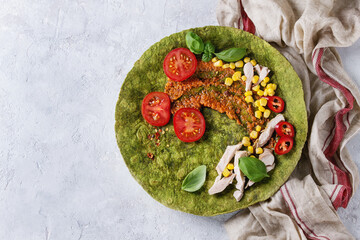 Green spinach matcha tortilla with ingredients for filling ready to wrap. Sweet corn, tomatoes, chili pepper, chicken meat, basil served over gray texture background and textile. Flat lay