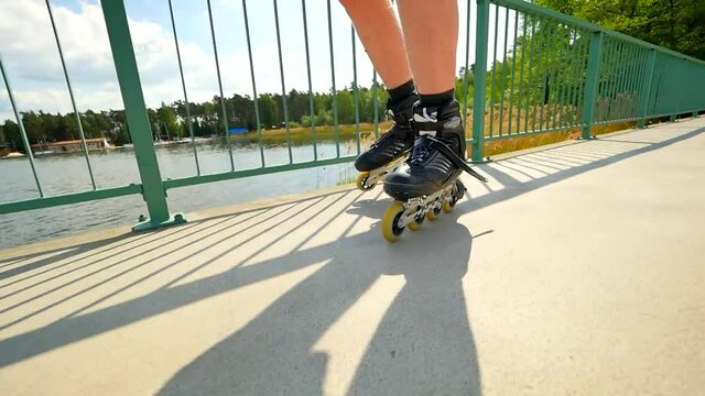 Front close view to inline skates riding on the bridge . Outdoor inline skating on smooth concrete ground on lake bridge. Light skin man in four wheel boots
