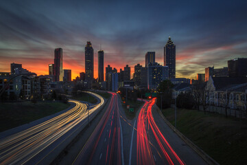 Long Exposure orange, pink, red, blue, purple sunset behind the Atlanta skyline from Jackson Street Bridge with streaked white and red car lights (company names have been edited out) - obrazy, fototapety, plakaty