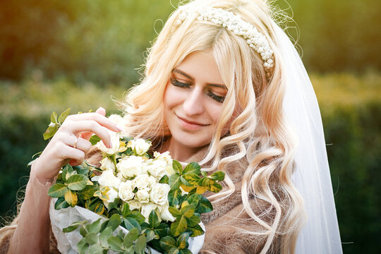 Beautiful young bride's wedding happy together in a park in white dress with veil and fur coat hugging a wedding bouquet, young family, looking lovingly