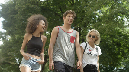 Three friends talking to each other as they walking together on a park trail. 
