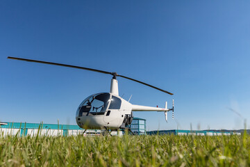 Small Robinson R22 light utility helicopter parked on grass airport. One of the world's most popular light helicopters with twin blades and a single engine - obrazy, fototapety, plakaty