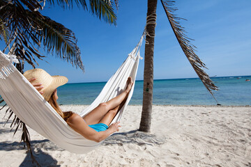 femme couchée dans un hamac sur la plage  avec un chapeau de paille