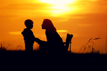 Naklejka na ściany i meble Silhouettes of mother and son at setting sun