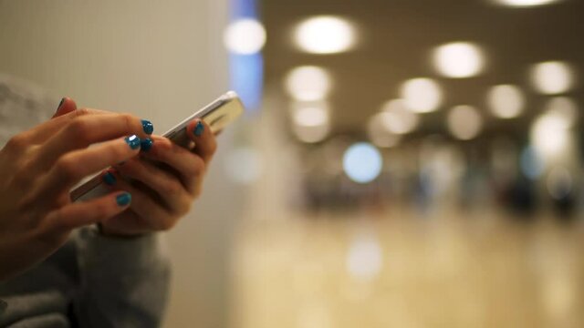 4k ultra hd small womans hands with blie color painted nails work with mobile phone in airport waiting hall. close-up. blurred departure zone background