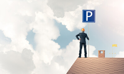Fototapeta premium Young businessman with parking sign standing on brick roof. Mixe