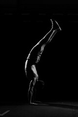 Fitness training. Male athlete walking on his hands or standing upside down in dark gym.