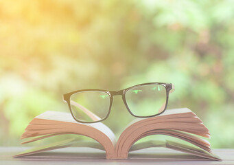 Book and glasses on wooden against nature background