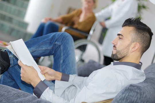 Man Reading Paperwork In Hospital Waiting Room