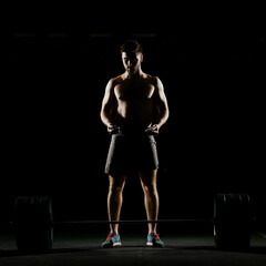 Fitness training. Man doing exercises or training with barbell in dark gym.