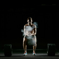 Fototapeta na wymiar Fitness training. Man doing exercises or training with barbell in dark gym.
