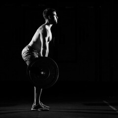 Fitness training. Man doing exercises or training with barbell in dark gym.