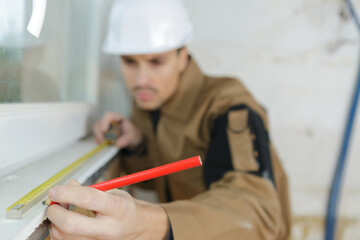 builder measuring a window using a tape measure and pencil