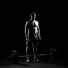 Fototapeta na wymiar Fitness training. Man standing with barbell in dark gym.