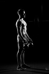 Fototapeta premium Fitness training. Man doing exercises with weights in dark gym.