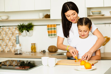 Mother teaches her daughter how to prepare breakfast from fruit, standing at white kitchen, Smiling and cutting orange. Family leisure at home
