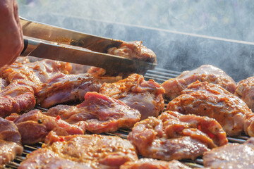 barbecuing on beautifull sunny day. turning meat steaks and chicken parts with clamps on bbq close-up