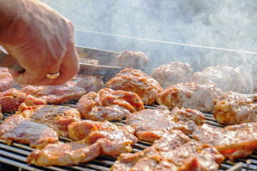 barbecuing on beautifull sunny day. turning meat steaks and chicken parts with clamps on bbq close-up