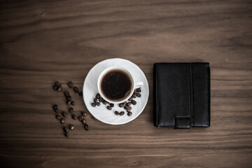 Saved coffee in a cup with a wooden background, green coffee around cups, coffee bean on wooden texture, wallet next to cups, businessman resting with coffee