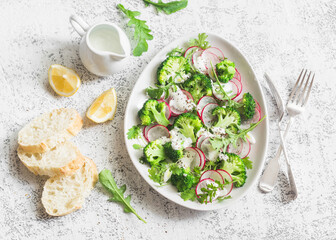 Spring broccoli and radish salad with yogurt sauce on a light background, top view. Delicious healthy vegetarian food concept