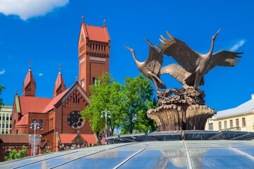 Church of Saints Simon and Helena (Red Church) and sculpture of bronze storks in Minsk, Belarus. - obrazy, fototapety, plakaty