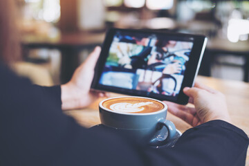 A woman holding and using black tablet with coffee cup on wooden table in cafe