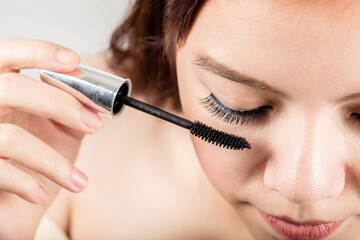 Woman applying black mascara on eyelashes with makeup brush