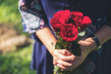 A woman holding red roses flower bouquet with green nature background