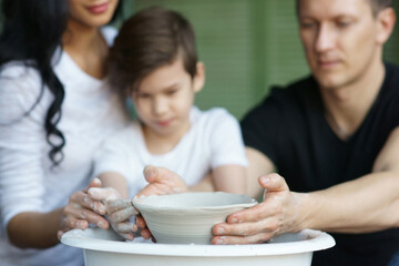 Parents teach their son to work on potter wheel. Shallow DOF. Focus on clay pot and dirty hands.