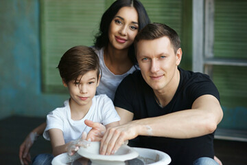 Young caucasian family working on potter's wheel. Handsome father, beautiful mother and young son. Pottery classes. Dirty Hands. Parents enjoying time together with their child.