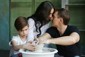 Young caucasian family working on potter's wheel. Handsome father, beautiful mother and young son. Pottery classes. Dirty Hands. Parents enjoying time together with their child.