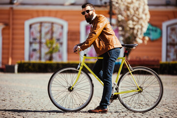 Naklejka premium Handsome young bearded man in sunglasses ride his bicycle on sunny city street