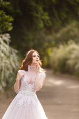 Fototapeta na wymiar Beautiful redhead Bride in fantastic wedding dress in blooming garden. Portrait in sunset light. Pretty young caucasian redhead girl walks in a garden and plays with her dress. Young princess