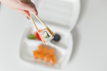 Hand keep roll with chopsticks, rolls, sushi. chopsticks, ginger, soy sauce in container delivery.