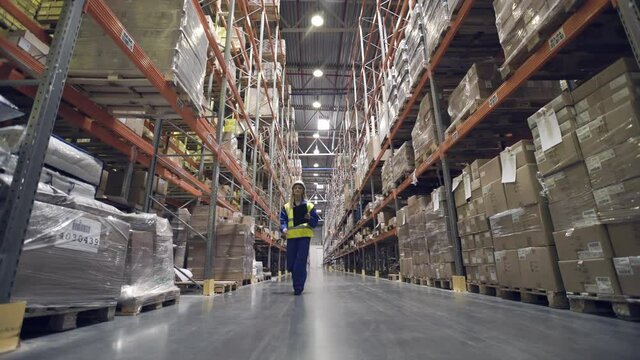 Female warehouse worker walks through rows of storage racks with merchandise