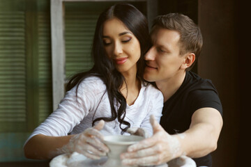 Romantic caucasian couple working on potter whel. Handsome man and pretty beautiful brunette woman making and sculpting clay pot together and hugging