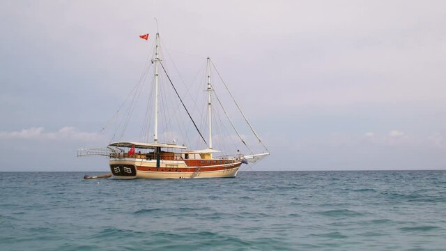 mooring touristic gulet with Turkish flags and lowered sails, near Mediterranean coastline