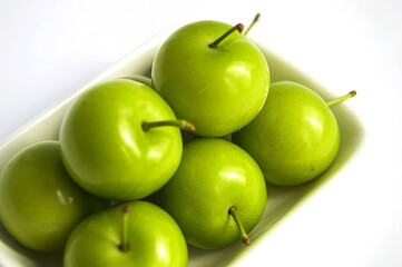 Green sour plums in the plate, plum pictures on the white ground,
Quality and natural life-giving green sour plums

