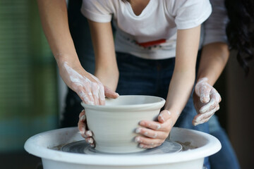 Mother teaches son to work on pottery wheel. Close up of dirty hands sculpting clay.