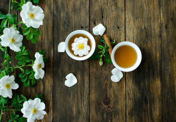 Cup of hot tea with rosehip and blooming flowers on old rustic wooden background