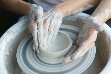 Couple working on pottery wheel. Top view of woman and man hands making ceramic pot or sculpting clay