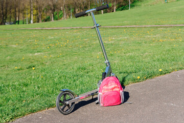 Scooter and backpack next to the green meadow.
